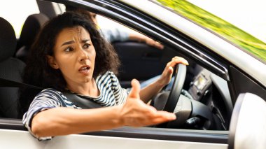 Öfkeli esmer kadın sürücü yolda kavga ediyor, arabanın camından bakıyor, el kol hareketi yapıyor ve bağırıyor, kadın trafiğe takılıyor ya da yolda kaza yapıyor, erkek arkadaşıyla seyahat ediyor, yan görüş