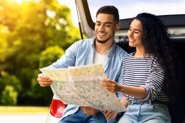 Orta doğulu çiftin yol haritasını izlemesi, mola vermeleri, arabayla seyahat etmeleri, kopyalamaları. Gülümseyen Arap adam ve güzel esmer kadın açık bir bagajda oturmuş, yeri kontrol ediyorlar.