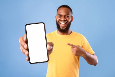 Yakışıklı, mutlu Afrikalı Amerikalı adam mavi ekranlı akıllı telefonu işaret ediyor. Web sitesi ya da yeni mobil uygulama için model. Cep telefonu görüntü şablonu. Reklam için alan