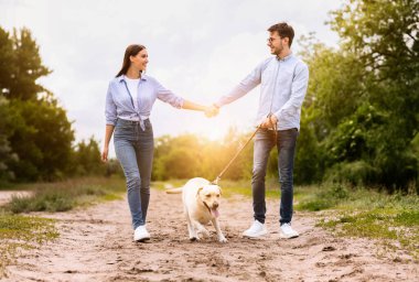 Köpek dostu randevu konsepti. Tasmalı iki genç insan birbirine bakıyor, el ele tutuşuyorlar.