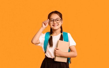 Okula Dönüş Konsepti. Neşeli Koreli Çocuk Kitap Tutuyor Sarı Stüdyo Arkaplanındaki Kamera Pozisyonuna Gülümsüyor.