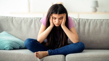 Covid bağlantılı gençlik depresyonu kavramı. Evdeki kanepede oturan mutsuz Hintli genç kız, iletişim ve yalnızlık eksikliğinden muzdarip, tecrit sırasında stresli hissediyor.