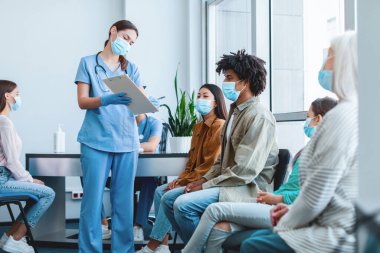 Coronavirus Aşı Kampanyası Konsepti. Kadın doktor ya da hemşire elinde bir not panosuyla klinikte bekleyen hastalarla konuşurken imzalamak için onay formu gösteriyor.