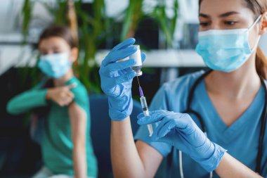Coronavirus bağışıklığı. Şırıngası olan ve şırıngayla şırınga ile şırınga aşısı alan mavi lateks eldivenli ve koruyucu maskeli hasta arka planda bekliyor.