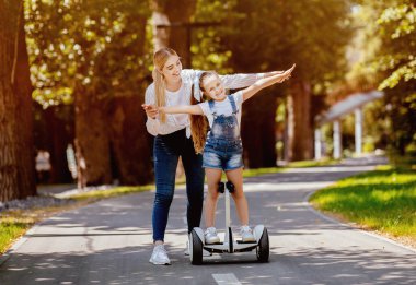 Anne, kızı Segway 'e binmeyi öğretiyor. Şehir parkında eğleniyor. Hafta sonu tatili konsepti. Boş Alan