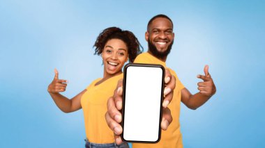 Şuna bak, cep telefonu ekran modeli. Pozitif Afro-Amerikan çift cep telefonuna işaret ediyor. Mavi arka planda boş ekran, seçici odaklanma. Mobil uygulama, web sitesi veya çevrimiçi reklam şablonu