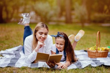Anne ve kızı kitap okuyor. Hafta sonunun tadını çıkarıyor. Şehir parkında aile pikniği yapıyorlar.