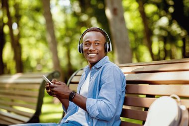 Milenyum siyahi adam parkta bankta oturuyor ve cep telefonundan müzik dinliyor.