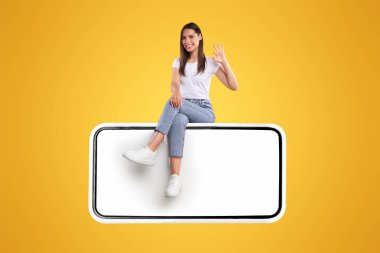 Beyaz ekranı boş ve jestli neşeli bir kadın, yeni uygulamayı veya web sitesini tavsiye eden mutlu genç bir bayan, turuncu arka planda izole edilmiş, yaratıcı bir kolaj.