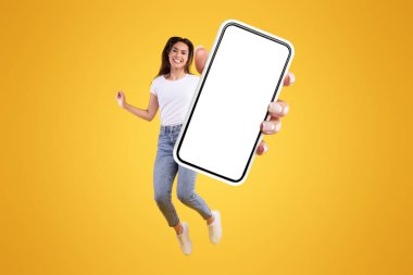 Cool Mobil Teklif Reklamı. Neşeli genç bayan, portakal rengi stüdyo arka planında parlayan, büyük, boş bir cep telefonu ekranı gösteriyor, yaratıcı kolaj. Mutlu kadın web sitesi tavsiye ediyor, bedava kopya alanı