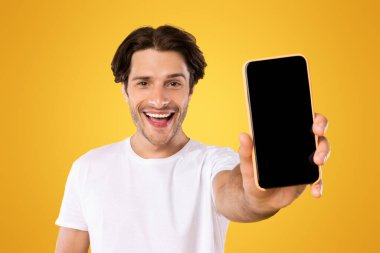 Mobil Uygulama İlanı. Akıllı Telefon Siyah Boş Ekran Uygulaması Gösteren Heyecanlı Adam Portresi Sarı Turuncu Stüdyo Arkaplanının Üzerinde Durmakta. Cep telefonu Görüntü Modifiye Et, Bu Web Sitesini Kontrol Et