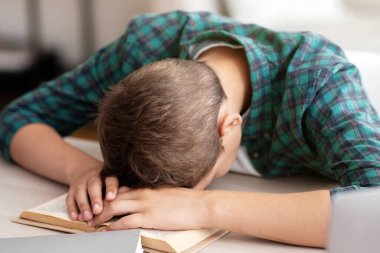 Ev ödevi yaparken masa başında uyuyan yorgun okul çocuğu.
