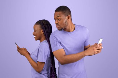 Profil yan görüntüsü: Meraklı siyahi adamın kız arkadaşlarına bakmaya çalışan akıllı telefonlu, elinde alet ve sohbet ile gülümseyen kadın sırt sırta duran çift, mor menekşe arka plan.