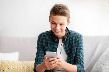 Akıllı telefon tutan mutlu genç adam, sosyal medyayı, ev içini, kopyalama alanını kontrol ediyor.