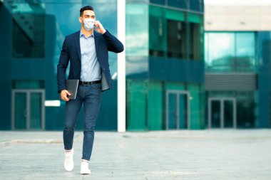 Ortadoğulu genç girişimci resmi kıyafetler içinde telefonda konuşuyor, iş görüşmesi yapıyor, maske takıyor, iş merkezinden çıkıyor, fotokopi alanı, iş yeri ve salgın hastalıklı bir panorama yaşıyor.