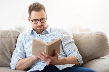 Boş zaman. Yakışıklı iş adamı evde kitap okuyor, kanepede oturuyor, gözlük takıyor, fotokopi çekiyor.