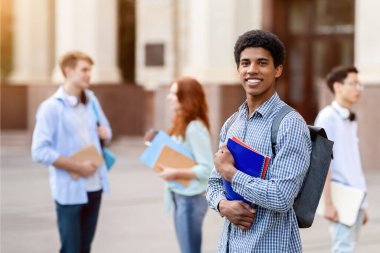 Açık üniversite binasının yanında duran sırt çantası ve kitaplarla poz veren mutlu Afrikalı Amerikalı öğrenci. Yurtdışında Çalışma Konsepti