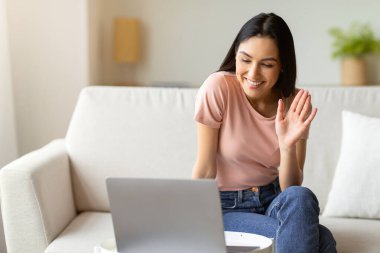 Bilgisayarla video görüşmesi yapan ve el sallayan bir kız. Uzaktan kumandalı koltukta oturuyor. Boş Alan