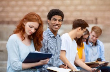 Sınavlara hazırlanan çok kültürlü öğrenciler üniversite binasının dışında oturuyorlar. Yurtdışında yüksek öğrenim. Seçici Odaklanma