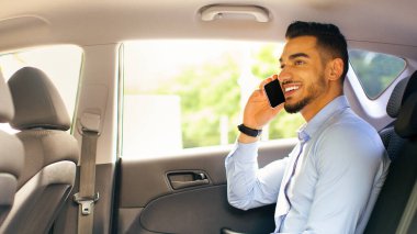 Neşeli genç Arap iş adamı havaalanına taksiyle giderken internetten çalışıyor. Mutlu CEO arabanın arka koltuğunda oturuyor, dizüstü bilgisayar kullanıyor ve telefon görüşmesi yapıyor.