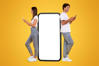 Harika bir uygulama. Büyük akıllı telefonlara yaslanan, boş telefonları kullanan neşeli adam ve sosyal medyada konuşan kadın, sarı turuncu arka planda duran, tüm vücudunu kaplayan, beyaz perdeli telefonları olan heyecanlı çift.