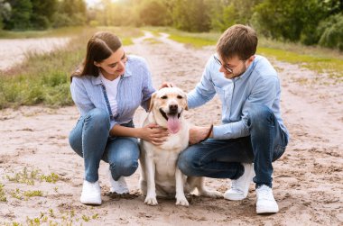 Mutlu genç bir çiftin portresi sevimli köpeklerine sarılıyor ve ona bakıyor, dışarıda yürüyor.