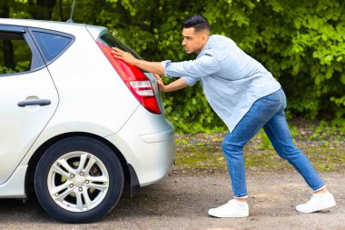Tarz sahibi günlük kıyafetli bir Arap, bozuk araba itiyor, yandan bakıyor. Orta Doğulu bir adam arkadaşlarıyla ya da sevgilileriyle seyahat ederken, kırsal yolda takılıp kalmış, otomobil hatchback 'i itmiş