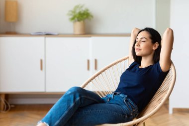 Hafta sonunun tadını çıkar. Kiz ellerini kafasinin arkasinda tutarak rahatliyor rahat koltukta oturuyor gözleri kapali evde dinleniyor. Boş Alan