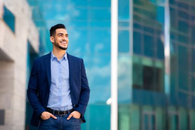 Yakışıklı, orta doğulu, şık takım elbiseli genç işadamı ofis merkezinde poz veriyor, başarılı bir iş toplantısından sonra gülümseyen Arap girişimci caddede duruyor, fotokopi alanına bakıyor.
