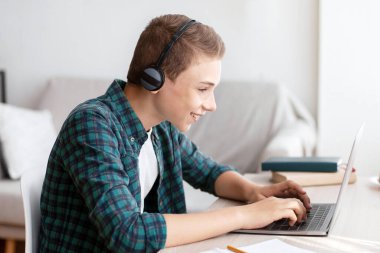 Evde kulaklığı olan neşeli bir okul öğrencisi bilgisayarda yazı yazıyor, online test yaptırıyor, boş alan var.