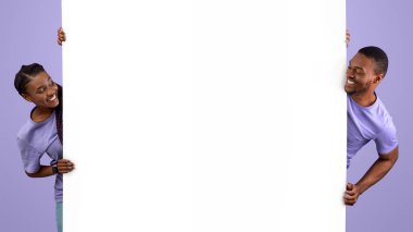 Gülümseyen genç siyahi insanlar ellerinde beyaz dikey reklam panosu tutuyorlar, metin ve tasarımın için bedava fotokopi alanı sunuyorlar, olumlu adam ve bayan pankarttan dışarı bakıyor, mor menekşe arka plan duvarı.