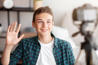 Genç blogcu, evinde kameraya el sallayarak suscrimlerine video çekiyor.