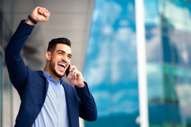 Mest olmuş Arap iş adamı iş ortağıyla telefonda konuşuyor, elini kaldırıyor, başarıyı kutluyor. Orta Doğulu girişimci asistanıyla akıllı telefondan konuşuyor, iyi haberler var.