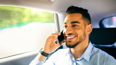 Ofise taksiyle giderken cep telefonuyla iş ortağıyla konuşan, arka koltukta oturan, yakın plan portresi çeken, fotokopi çeken mutlu bir orta doğulu genç adam. İş adamı yaşam tarzı konsepti