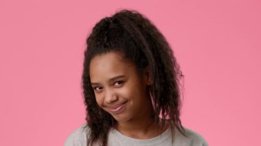 Kıvırcık saçlı neşeli bir Afro-Amerikan genci canlı pembe bir arka plana karşı poz verirken neşeli bir gülümseme sergiliyor. Parlak ayarı gençlik enerjisini ve cazibesini arttırıyor..