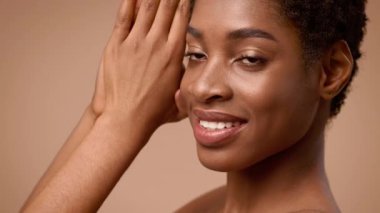 Genç bir Afrikalı Amerikalı kadın ışıl ışıl bir gülümsemeyle güzelliğini sergiliyor. Nazikçe poz verir. Özgüvenini ve zarafetini yumuşakça bulanık bir arka plana vurgular..