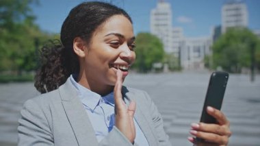 Takım elbiseli kendine güvenen Afrikalı Amerikalı bir kadın kalabalık bir şehir parkında dikilirken akıllı telefonuna bakar..