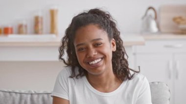 Neşeli bir Afro-Amerikalı genç kız kanepede tek başına oturur ve keyifle güler. Sakin ve şık bir iç mekanla çevrili, hafif bir anı kucaklıyor..