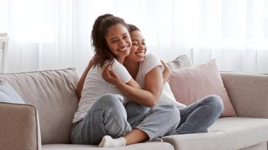 İki Afrikalı Amerikalı kız kardeş evlerindeki bir kanepede rahatça oturuyorlar. Gülücükleri ve kahkahaları paylaşırlar, birbirlerine eşlik ederken güçlü bir sevgi ve kardeşlik bağı gösterirler..