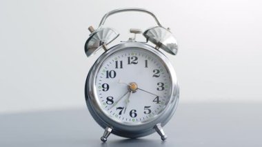 Şık bir çalar saat huzurlu bir yatak odasındaki komodinin üzerinde duruyor. Parlak metalik kaplaması ışığı yansıtıyor, dinlenmek ve dinlenmek için mükemmel sıcak ve davetkar bir atmosfer yaratıyor..