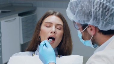 Bir dişçi, çağdaş bir diş kliniğinde hastaya bakım sağlar. Kadın hasta ağzı açık bir şekilde oturuyor ve dişçi sağlık hizmetlerinin kalitesini gösteren bir muayeneye hazırlanıyor..