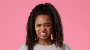 Güzel bir Afro-Amerikalı genç, dağınık bukleli saçlarıyla, şaşkın bir yüz ifadesini sergiliyor. Çarpıcı pembe arkaplan canlı bir karşıtlık ekler.