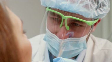 Bir dişçi, modern bir klinikte diş muayenesi sırasında hastayla iletişim kurarak, güvenli bir ortamda sağlık ve hasta rahatlığının önemini gösterir..