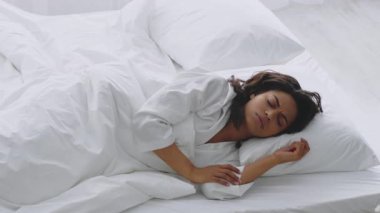 Genç bir Afrikalı Amerikalı kadın kendini hasta hissediyor, yatak odasında dinleniyor, bembeyaz bir yatağa rahatça yerleşmiş. Bornoz giyiyor.