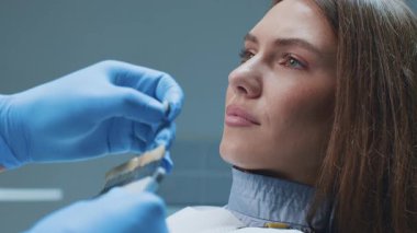 Bir dişçi diş aletlerini kullanarak dişlerini incelerken bir hasta kendinden emin bir şekilde gülümser. Modern klinikte, optimum diş bakımı için gelişmiş sağlık teknikleri vurgulanmaktadır..