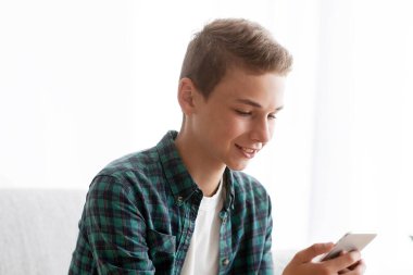 Evdeki kanepede oturan ve cep telefonu kullanan bir genç.