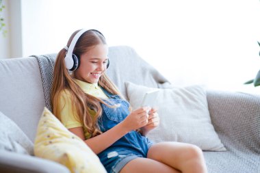 Günlük Yaşam Konsepti. Liseli kız evde koltukta dinleniyor, Müzik dinliyor ve cep telefonuyla sohbet ediyor.