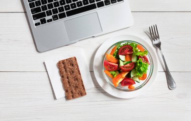 Ofiste sağlıklı bir iş yemeği, dizüstü bilgisayar klavyesinin yanındaki tahta masadaki sebze salatası manzarası..