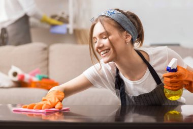 Mutlu genç ev hanımı evde bahar temizliği yapıyor, masadan toz temizliyor, paçavra ile yüzeyi yıkıyor, kapatıyordu.