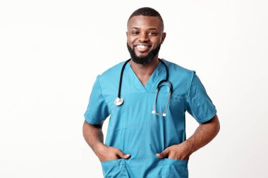 Steteskoplu neşeli Afrikalı Amerikalı doktor ellerini beyaz arka plandaki ceplere sokuyor.